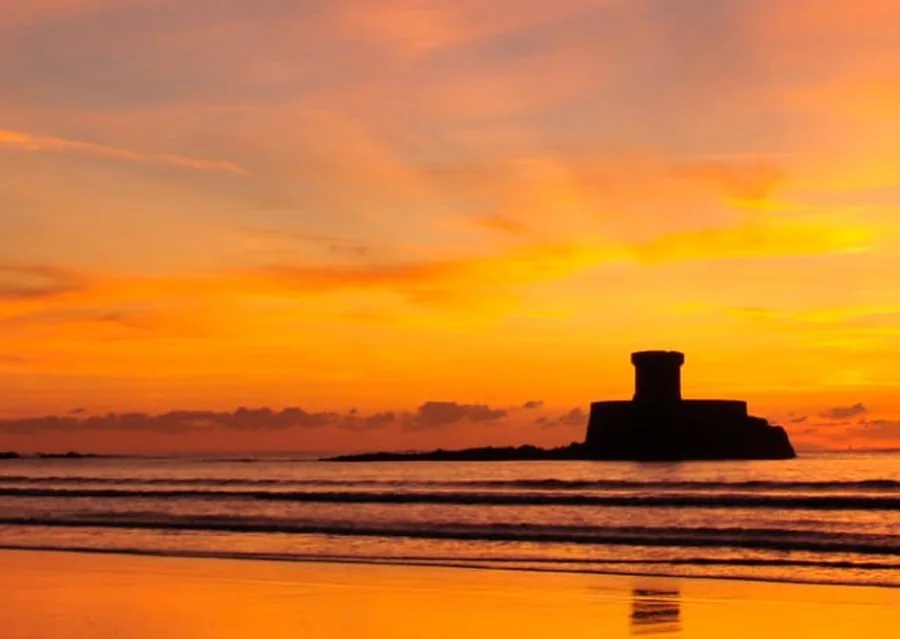 Jersey coastline at sunset with a coastal tower silhouetted offshore